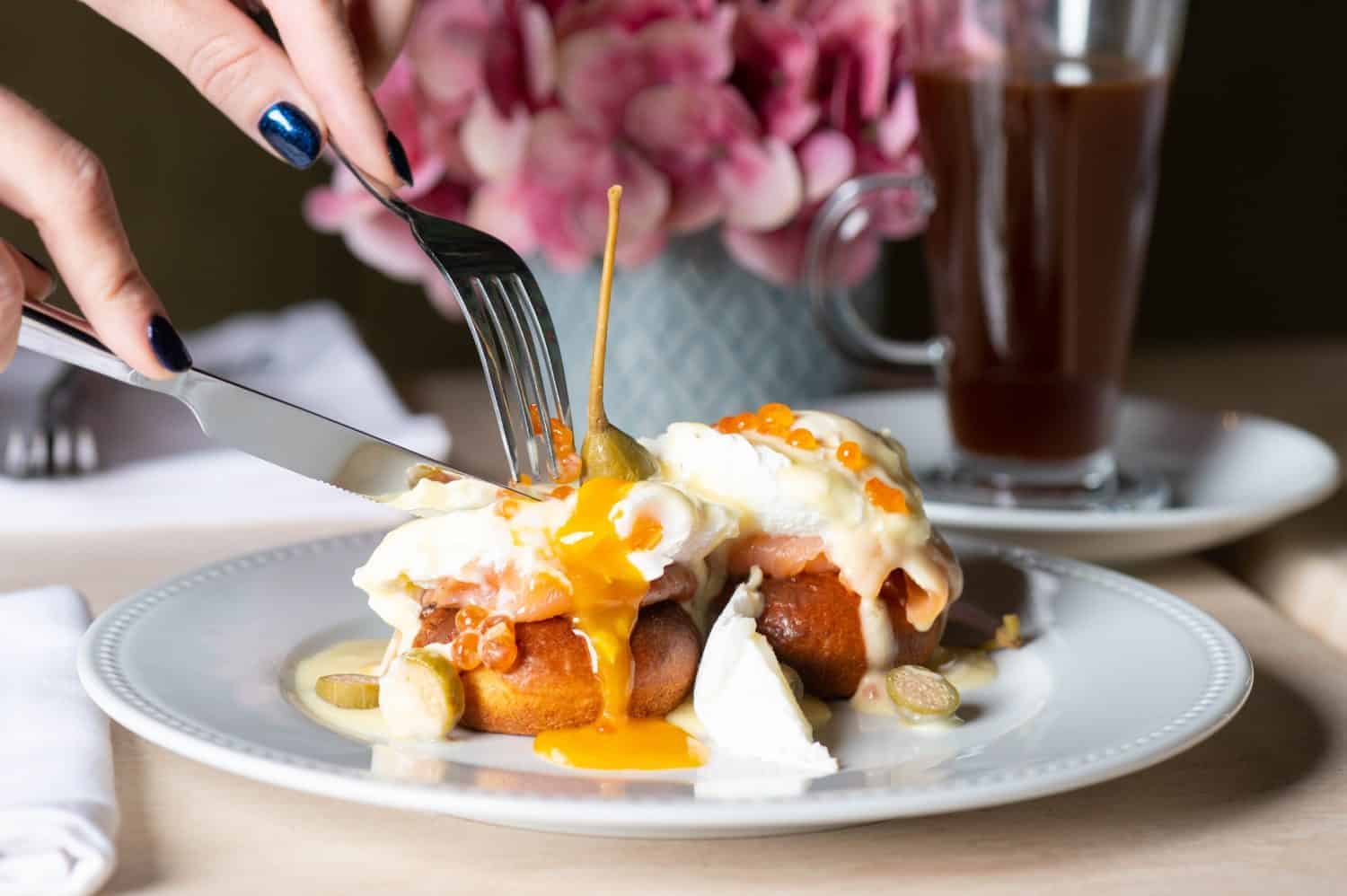 Girl eating eggs benedicts with smoked salmon, capers and salmon caviar for breakfast